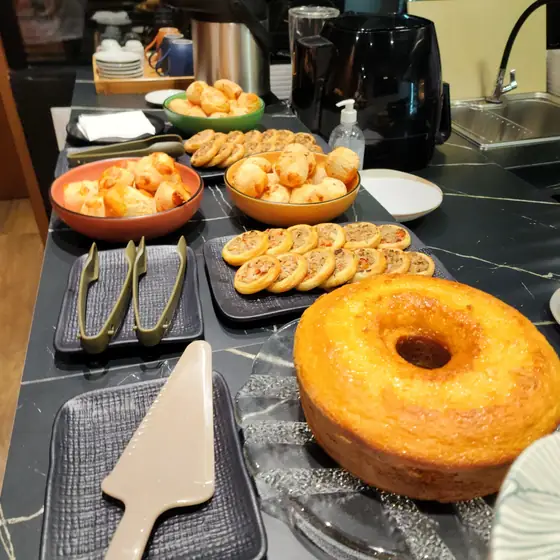 Bancada do coffee break com pães de queijo, esfihas abertas e bolo no Espaço Convivium