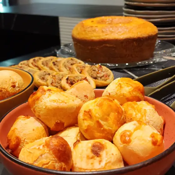 Pães de queijo e esfihas abertas no coffee break do Espaço Convivium, com bolo ao fundo