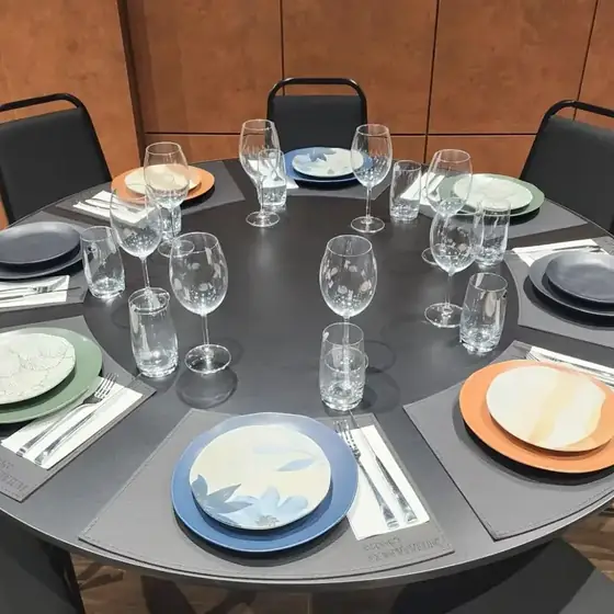 Mesa redonda posta com pratos coloridos, taças e jogo americano com a marca Espaço Convivium